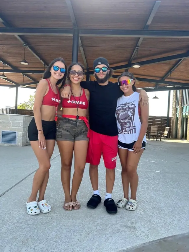 Four guards standing together under the shade structure at a community pool.